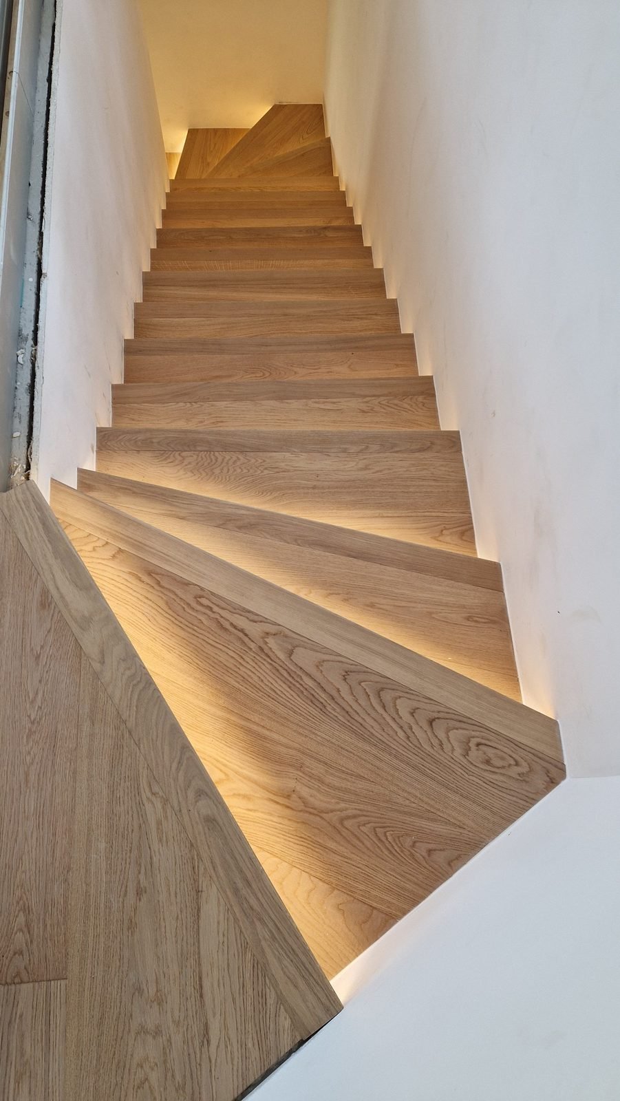 Escalier en chêne vu du palier, marches éclairées par des rubans lumineux
