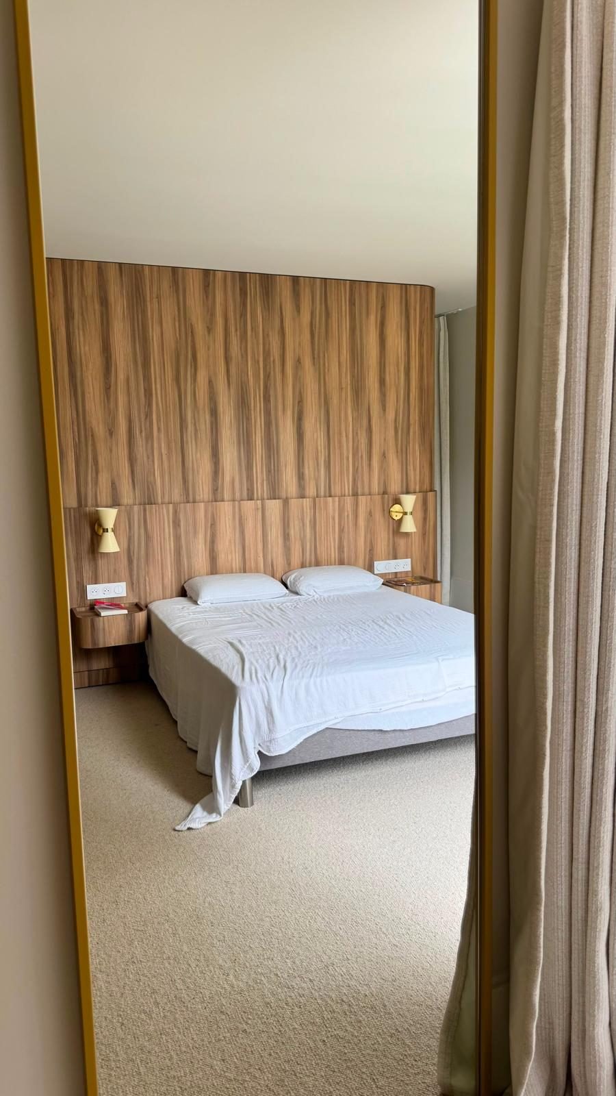 Chambre en moquette beige vue dans un miroir, tête de lit en bois
